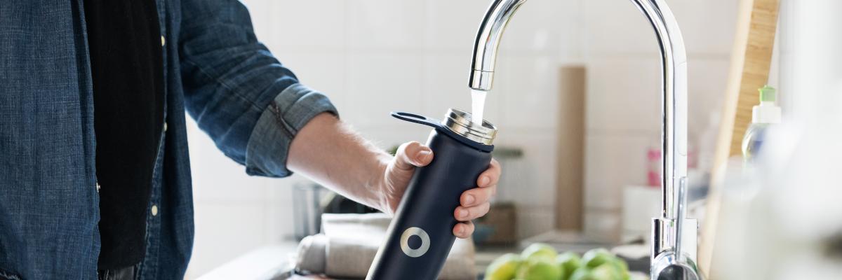 Person filling a water bottle at a kitchen sink faucet 