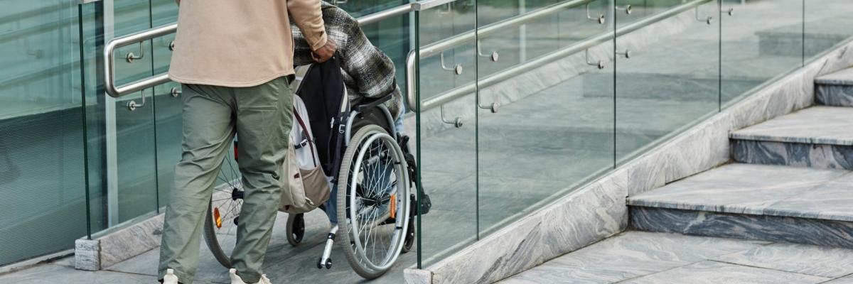 Man pushing a person in a wheelchair up a ramp