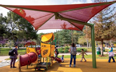 large shade structure over a playground with children and parents
