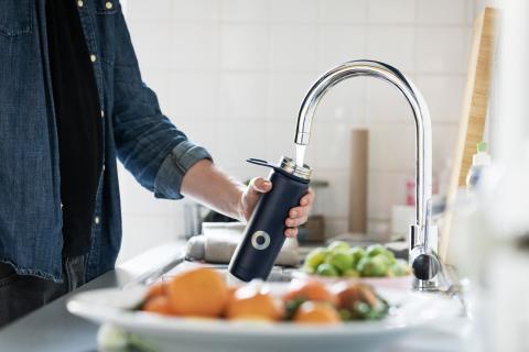 Person filling a water bottle at a kitchen sink faucet 